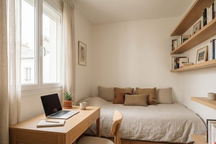 Chambre transformée en bureau le jour avec un bureau en bois, un ordinateur portable et un lit habillé comme un canapé
